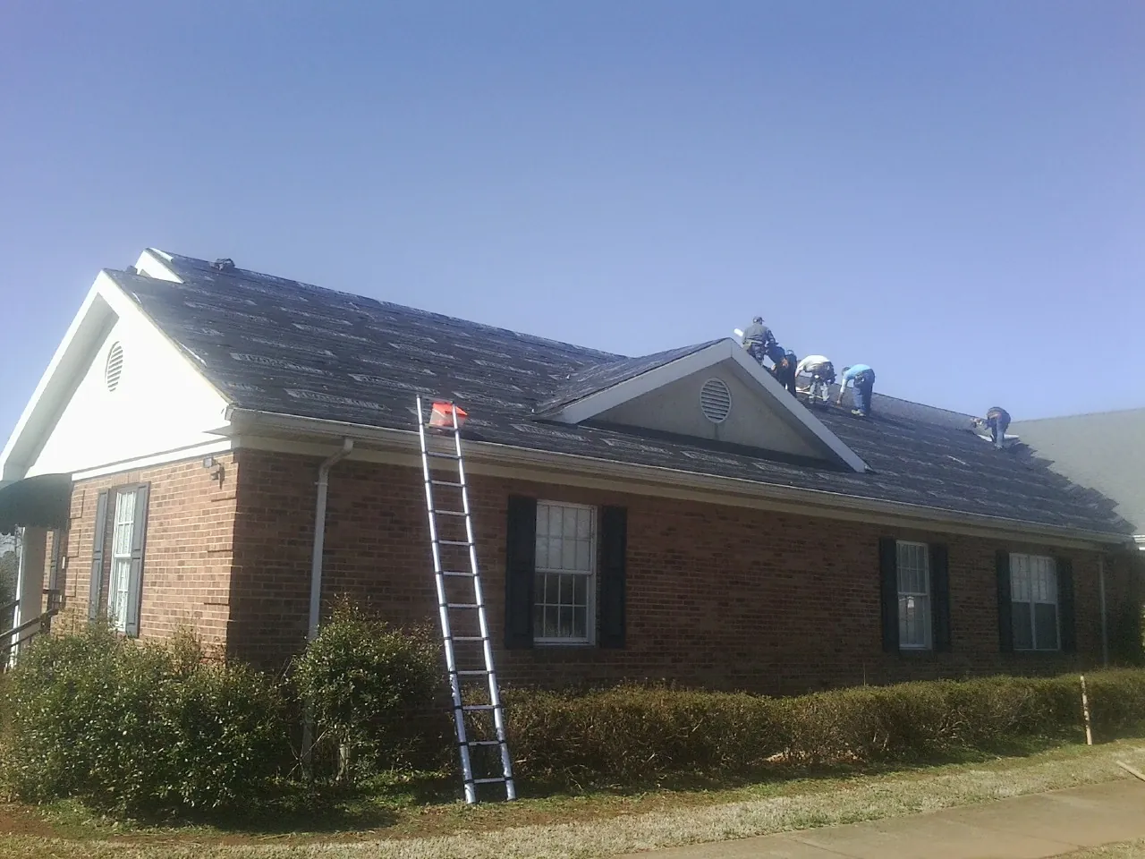 Crew tearing shingles off a brick ranch roof with a ladder set — Emergency Roof Repair work by our crew in Chico