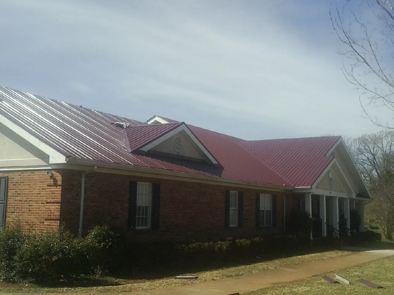 Red metal roof with gabled entries on a long brick building, from a Hail Damage Roof Repair job in Chico